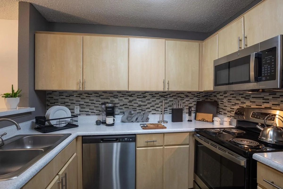 Kitchen with stainless steel appliances and tile backsplash at Village Green of Bear Creek in Euless, Texas