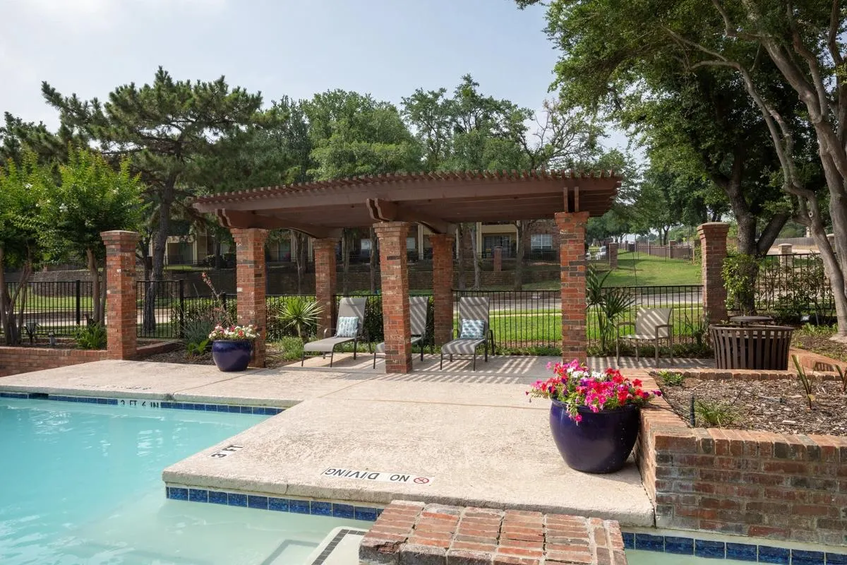 Shaded pergola and poolside lounge area at Village Green of Bear Creek in Euless, Texas